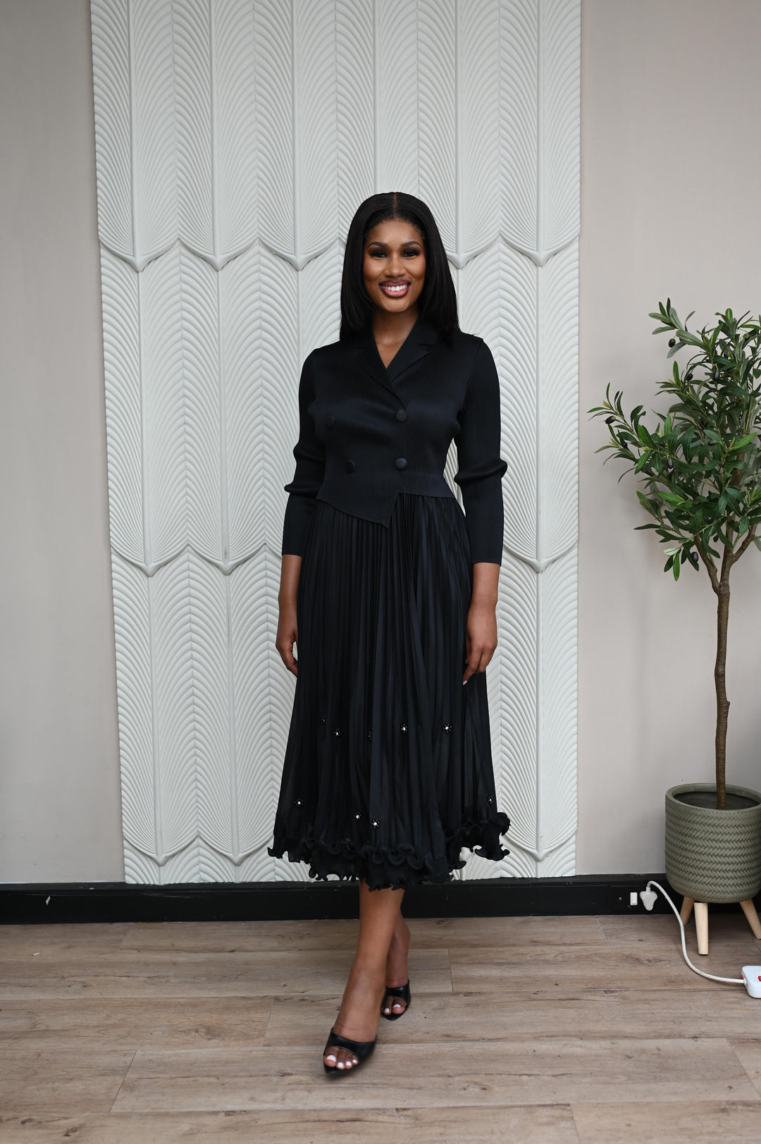The Executive Muse Dress in black, front view showing the ruffled pearl-embellished hem